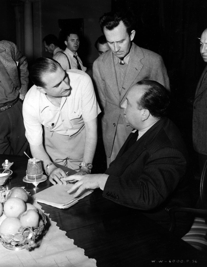 Alfred Hitchcock (left) discusses trick photography with aviator and stunt flier Paul Mantz (left), while assistant director Eddie Bernoudy (center) looks on.