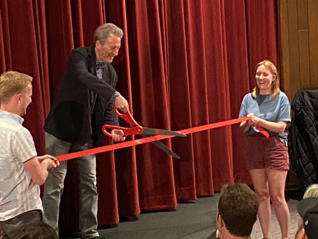 Ken Kwapis cuts a large ribbon with a large pair of scissors