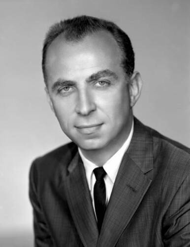 Black and white photograph of a man in a suit jacket, white shirt, and black tie